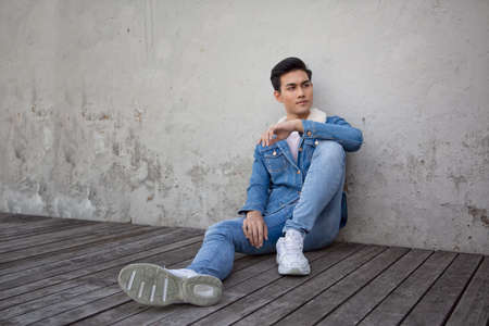 Handsome young man posing on vintage dark background. Portrait of satisfied Asian man against wall....