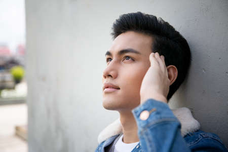 Handsome young man posing on vintage dark background. Portrait of satisfied Asian man against wall. Close up face of fashionable Asian man on wall background.の写真素材