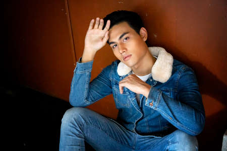 Handsome young man posing on vintage dark background. Portrait of satisfied Asian man against wall....