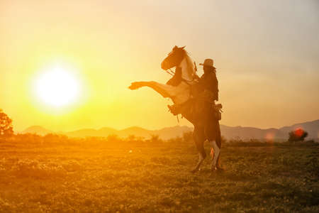 Cowboy riding a horse carrying a gun in sunset with mountain, Western cowboy portrait