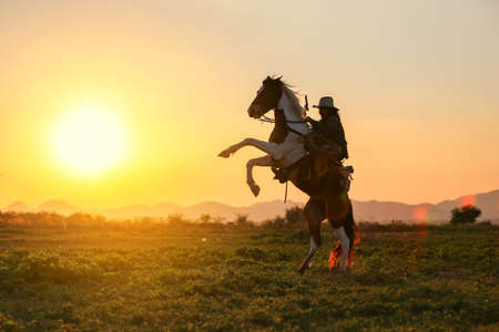 Cowboy riding a horse carrying a gun in sunset with mountain, Western cowboy portrait