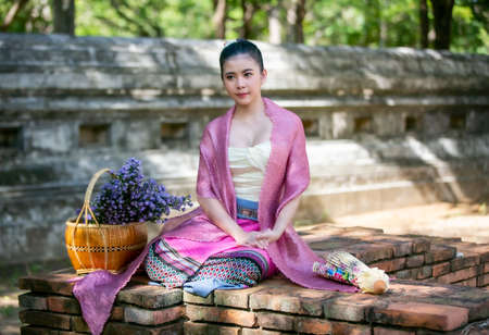 Portrait of an Smiling Young Woman in Thai Lanna Traditional Clothes are Smiling Young Woman Holding Flower Basket and and hold umbrella Against Thailand Templeの写真素材