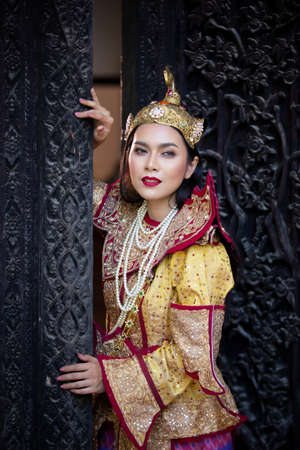 Portrait of an Asian Women in Mandalay, Myanmar Woman with golden Traditional Clothes are Standing Against Art Carving Wooden Door.の写真素材