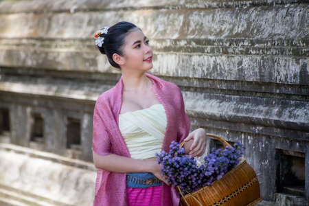 Portrait of an Smiling Young Woman in Thai Lanna Traditional Clothes are Smiling Young Woman Holding Flower Basket and and hold umbrella Against Thailand Templeの写真素材
