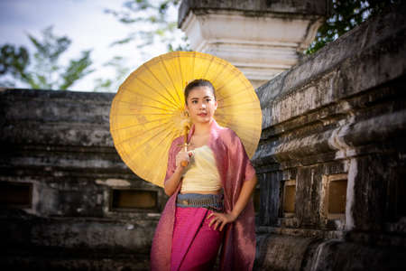 Portrait of an Smiling Young Woman in Thai Lanna Traditional Clothes are Smiling Young Woman Holding Flower Basket and and hold umbrella Against Thailand Templeの写真素材