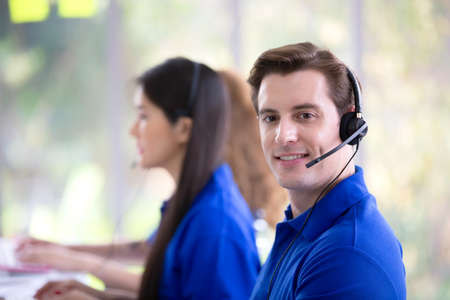 Call center staff in blue T-shirt accompanied by her team. Smiling customer staff support operator...