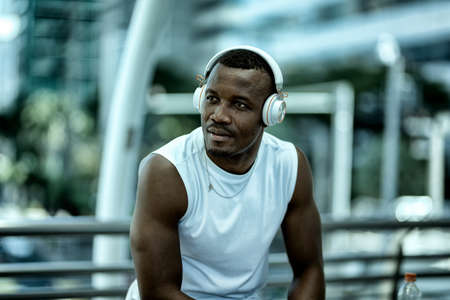 african-american man in sportswear in wireless headphones listening music and enjoying music on background of stairsの写真素材