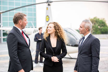 confident business people standing against his private helicopter at landing airport. Professional...