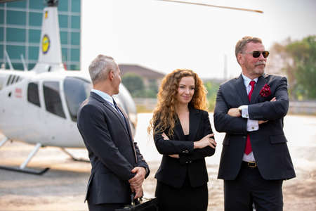 confident business people standing against his private helicopter at landing airport. Professional...