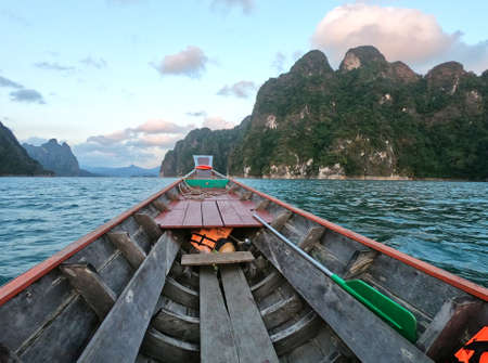 A longtail boat floats on the water, with the front facing the sea and the rear facing the mountains.の写真素材