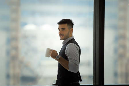 Happy young man is drinking coffee and smiling while standing at the cafÃ©