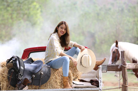 A woman in a cowgirl style sits in a horse ranch with a western farm environment.の写真素材