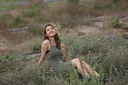A beautiful woman with long hair in a dress sitting on a meadow and flowers in the evening light.の写真素材