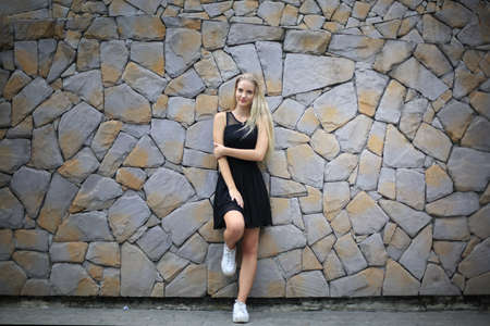 Portrait of Beautiful blonde hair girl on black dress against stone wall as fashion portrait outdoor.の写真素材