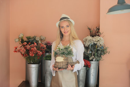 Beautiful blonde hair girl standing with confidence in front of flower in open retails flora shop. Small business owner concept.の写真素材
