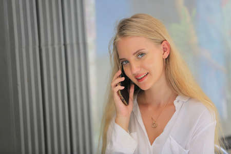 Beautiful blonde hair girl speaking on mobile phone with laptop on table outside coffee shop.の写真素材