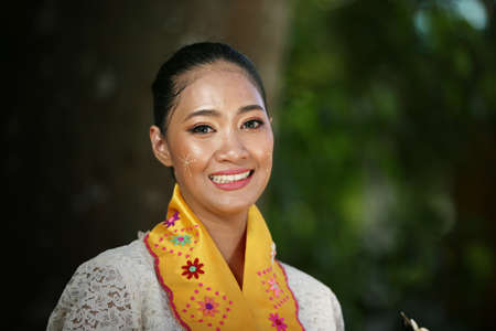 Portrait of a Burmese girl with traditional Thanaka face painting in front of golden Pagodaの写真素材