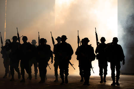 Silhouettes of army soldiers in the fog against a sunset, marines team in action, surrounded fire and smoke, shooting with assault rifle and machine gun, attacking enemyの写真素材