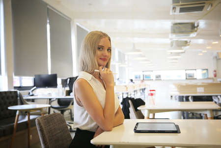 Young and cheerful woman working on digital tablet using wireless internet while sitting relaxed at cafe. Concept of leisure, freelance and mobile workの写真素材