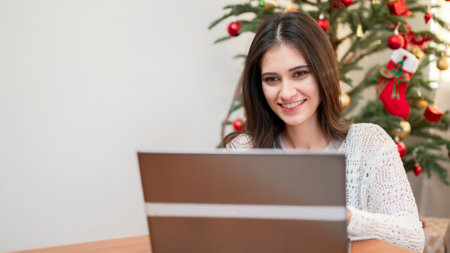 smiling young woman using laptop against Christmas tree.の写真素材