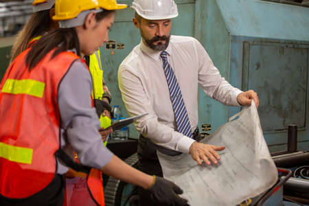 Male engineer and Industrial workers in Hard Hats Discuss New Project while Using Laptop. They Make Showing Gestures.They Work in a Heavy Industry Manufacturing Factory.の写真素材