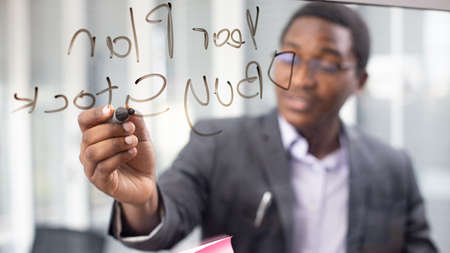 African American young man writing note on a transparent wipe board and thinking of a solution for...