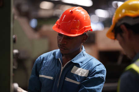 Portrait of Professional Heavy Industry Engineer / Worker Wearing Safety Uniform, Goggles and Hard Hat. In the Background Unfocused Large Industrial Factoryの写真素材