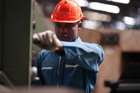 Portrait of Professional Heavy Industry Engineer / Worker Wearing Safety Uniform, Goggles and Hard Hat. In the Background Unfocused Large Industrial Factoryの写真素材