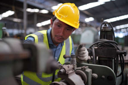 Male engineer metalworker industrial experienced operator technician worker in safety hard helmet working on lathe machine, professional man in industry technology manufacturing factory workshopの写真素材