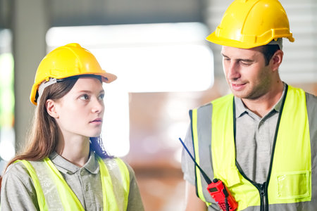 Young female engineer and male supervisor discussing construction plan in a warehouse.の写真素材