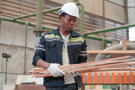 African American worker examining stock of timber while working at wood warehouse.