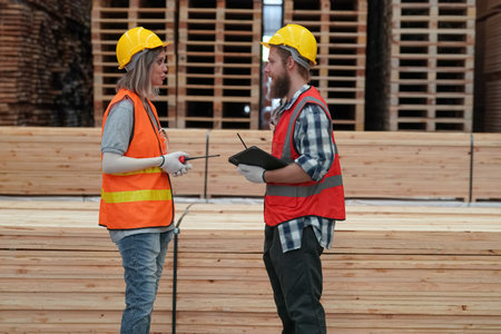 Side view of a Caucasian male and female construction workers discussing over clipboard in a warehouseの写真素材