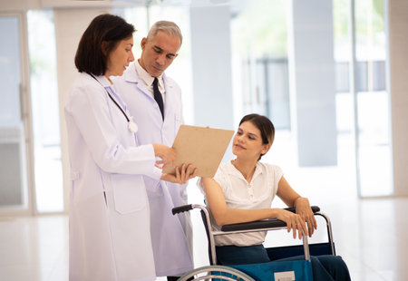Doctor and patient discussing something while sitting in a wheelchair at the hospitalの写真素材