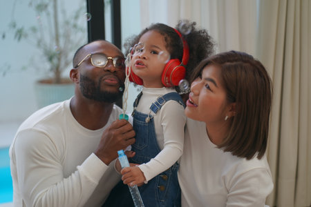 Shot of joyful parents with their little daughter sitting on floor inside living room in sunny day.. Little girl with special needs enjoy spending time with family.の写真素材