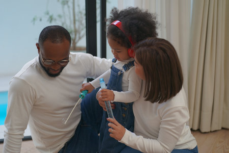 Shot of joyful parents with their little daughter sitting on floor inside living room in sunny day.. Little girl with special needs enjoy spending time with family.の写真素材