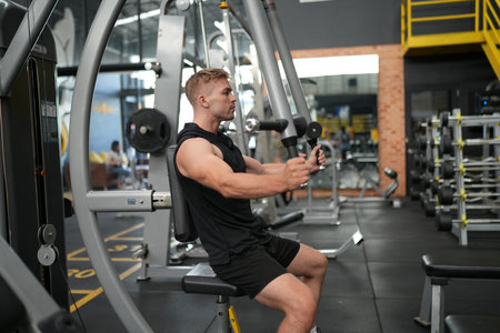 Muscular Young Man Doing Heavy Weight Exercise For Back On Machine In The Gym