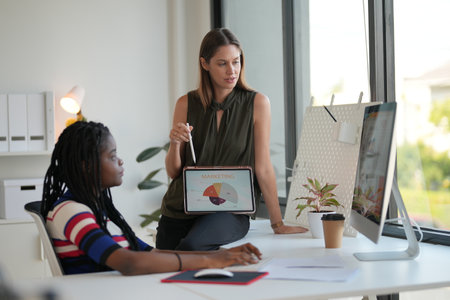 Portrait of two young businesswomen working together in office. They are sitting at the desk and...