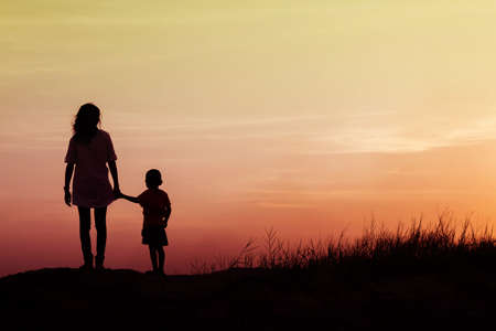 Mother encouraged her son outdoors at sunset, silhouette conceptの写真素材