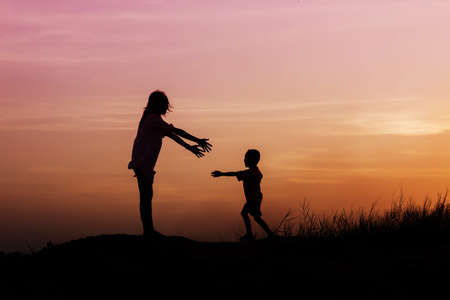 Mother encouraged her son outdoors at sunset, silhouette conceptの写真素材