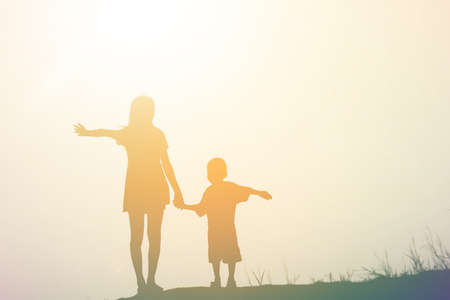 Mother encouraged her son outdoors at sunset, silhouette conceptの写真素材