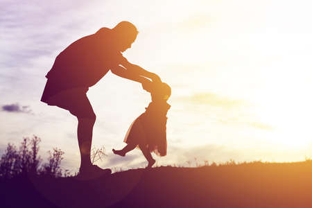 Silhouettes of mather and little daughter walking at sunsetの写真素材