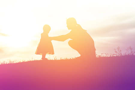 Silhouettes of mather and little daughter walking at sunsetの写真素材