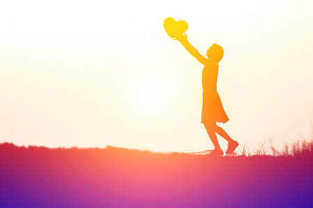 a silhouette of a happy young girl child  in hands give heart the  sunset.の写真素材