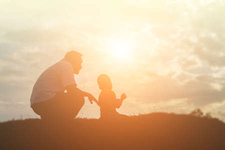 Silhouettes of father and little daughter walking at sunsetの写真素材