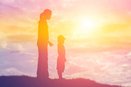 a silhouette of a happy young girl child the arms of his loving mother for a hug, in front of the sunset in the sky on a summer day.の写真素材