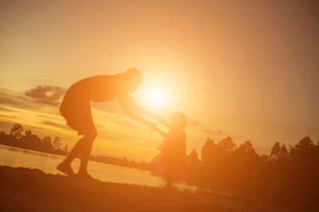 Silhouettes of mother and little daughter walking at sunsetの写真素材