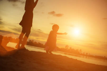 Silhouettes of mother and little daughter walking at sunsetの写真素材
