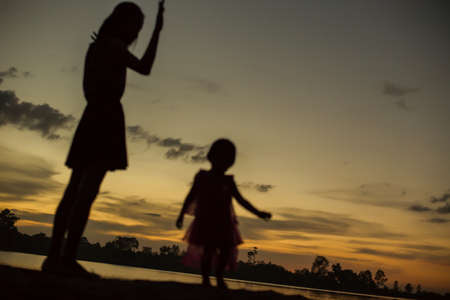 Silhouettes of mother and little daughter walking at sunsetの写真素材