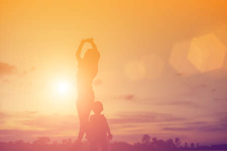 Silhouettes of mother and little daughter walking at sunsetの写真素材
