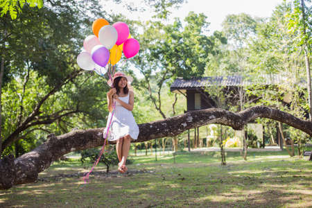 Young teen girl sitting on tree and holding balloons in handの写真素材